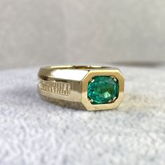 a gold ring with a green stone in the center on a white cloth covered surface