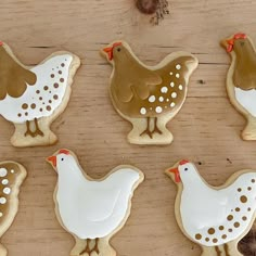 six decorated cookies in the shape of chickens and hens on a wooden table top