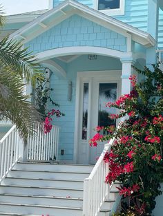 a blue house with pink flowers on the front steps