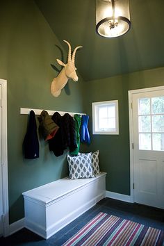 a room with green walls, white bench and deer head mounted on the wall above it