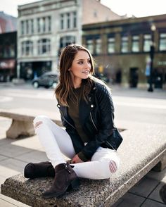 a woman sitting on top of a cement bench next to a building and wearing white pants