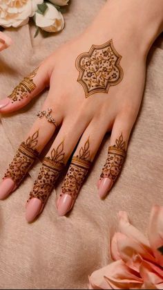 a woman's hand with henna tattoos on it and flowers in the background