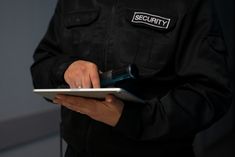 a security officer holding a tablet computer in his hands and writing on the screen with a pen