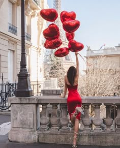 a woman in a red dress is holding up some heart shaped balloons on the street