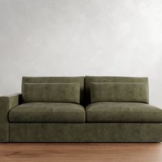 a green couch sitting on top of a wooden floor next to a white wall in an empty room