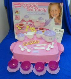 a pink toy table with purple cups and saucers on it in front of a blue backdrop