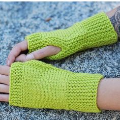 a person wearing green knitted arm warmers on top of a cement surface with their hands in the air