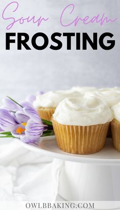 two frosted cupcakes sitting on top of a white cake plate with purple flowers