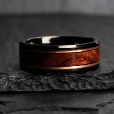 a wooden ring sitting on top of a piece of black wood with a brown stripe