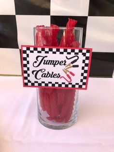 some red candles are sitting in a glass on a table with a sign that says jumper cables