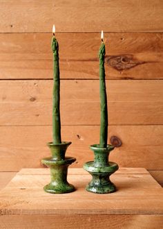 two green candles sitting on top of a wooden table