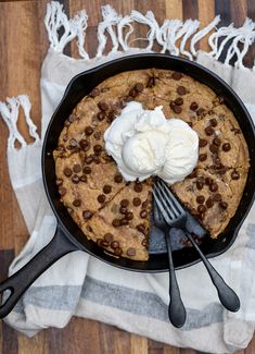 a skillet with chocolate chip cookie and whipped cream on top next to utensils