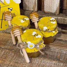 three honey jars with bees and daisies on them, tied to wooden pegs