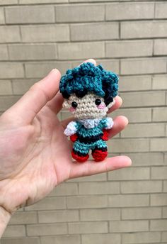 a small crocheted doll is held up in front of a brick wall,