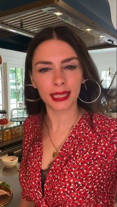 a woman wearing large hoop earrings and a red shirt in a kitchen with food on the counter