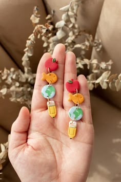 a person is holding some fruit earrings in their left hand and the other one has an apple on it