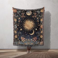 a woman is standing in front of a tapestry with the sun and moon on it