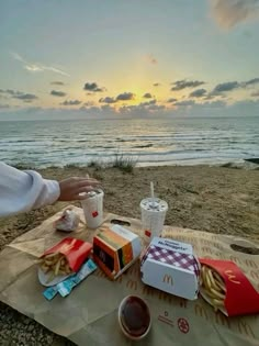 a person sitting at a picnic table on the beach with food and drinks in front of them