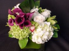 a vase filled with white and purple flowers on top of a black table next to green leaves