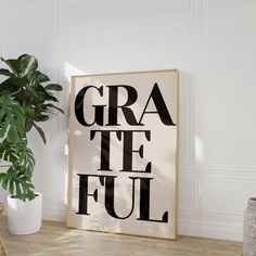 a black and white poster with the words gra te ful on it next to a potted plant