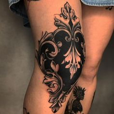 a woman's leg with tattoos on it and an ornate heart tattoo on the thigh