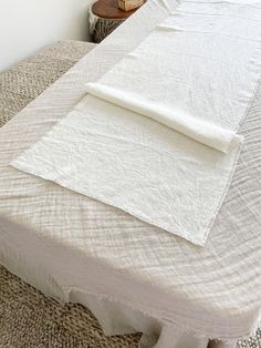 an unmade bed with white linens and a basket on the end table next to it