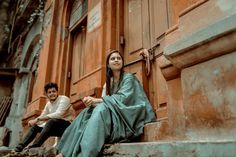 two people sitting on the steps in front of an old building