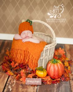 a baby sleeping in a basket with fall leaves and pumpkins