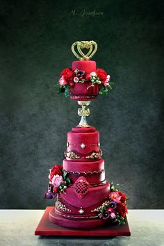 a three tiered red wedding cake with flowers and hearts on the top, sitting on a table