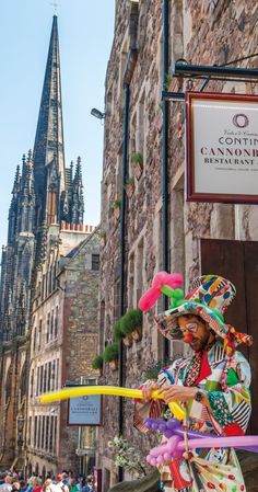 a man in costume juggling on the street with people walking around him and buildings in the background