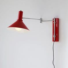 a red wall mounted lamp on the side of a white wall next to a light fixture