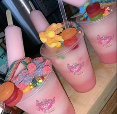 three cups filled with candy and gummy bears on top of a wooden table next to an ice cream machine