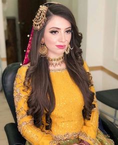 a woman in yellow dress sitting on a chair with long dark hair and wearing gold jewelry