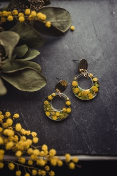 two pairs of earrings sitting on top of a table next to yellow flowers and greenery