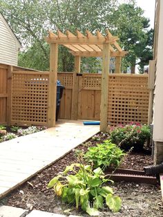 a wooden walkway leading to a garden with flowers and plants in the foreground, next to a fence