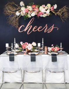 a table topped with flowers and candles next to a chalkboard sign that says cheers