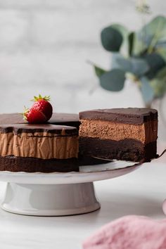 a piece of chocolate cake on a white plate with a strawberry in the middle and one slice missing