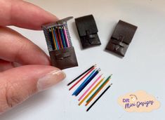 a hand holding a small piece of leather with colored pencils next to it and other items