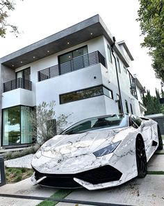 a white sports car parked in front of a modern house with large windows and balconies