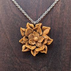 a wooden flower pendant on a chain with a silver plated necklace attached to it