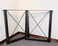 two black metal and glass side tables against a white wall in an empty room with carpeted flooring