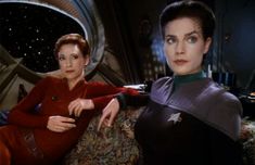 two women sitting on a couch in front of a star trek ship, one pointing at the camera