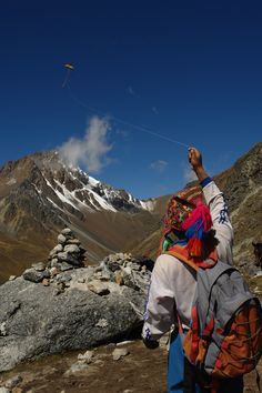 a person flying a kite on top of a rocky mountain range with snow covered mountains in the background