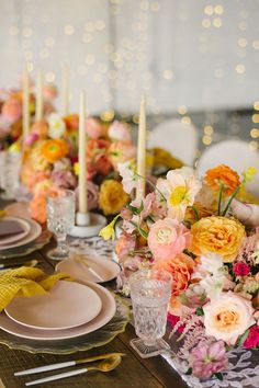 the table is set with plates and flowers on it, candles are lit in the background