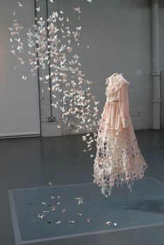 a dress made out of white paper flying in the air next to a wall with flowers on it