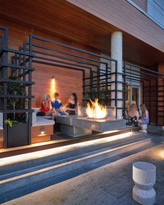 people sitting on benches in front of a building with lit up plants and fire pits