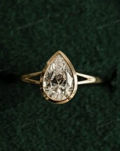 an engagement ring with a pear shaped diamond in the center on a green carpeted surface