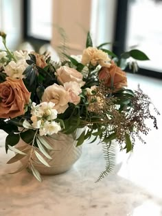 a vase filled with lots of flowers sitting on top of a marble counter next to a window