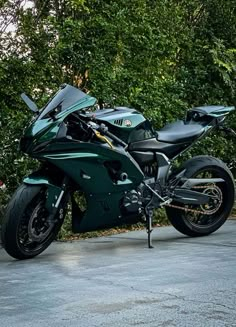 a green motorcycle parked on the side of a road next to some bushes and trees