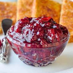 a glass bowl filled with cranberry sauce on top of a white plate next to slices of cake